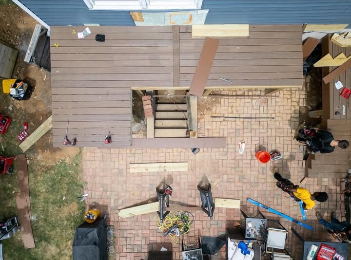 Aerial view of people building a wooden deck over a brick patio, with tools and materials scattered around.