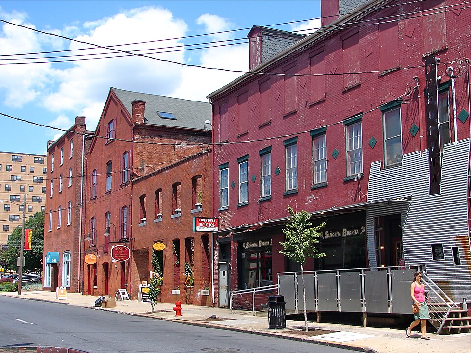 Teller_Bros_HD_Lancaster_PA-1 A woman jogs past red brick buildings and shops on a sunny city street with blue sky and clouds.