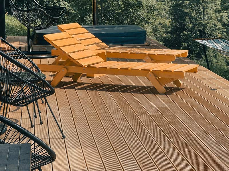 Two wooden lounge chairs on a deck with trees and a hammock in the background.