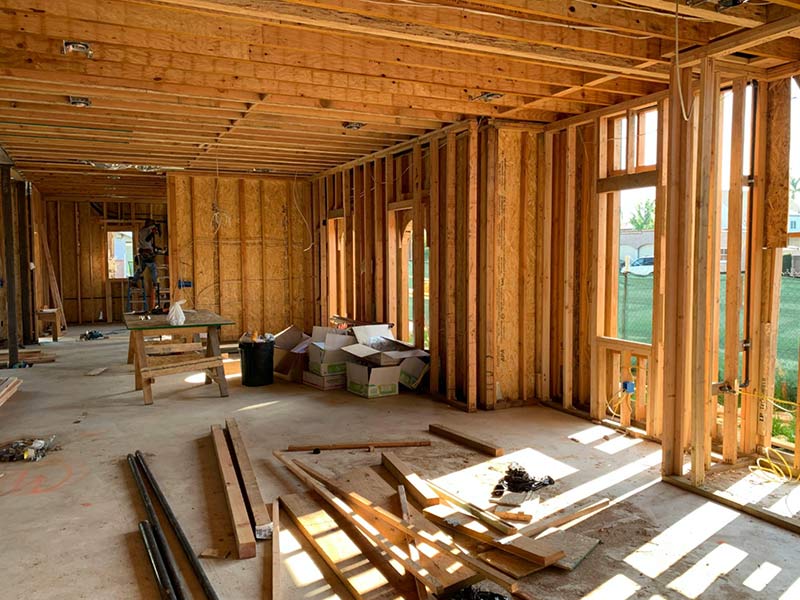 Interior of a house under construction with exposed wooden framing, scattered tools, and boxes.