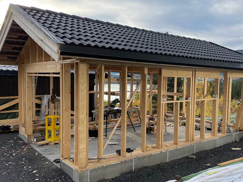 Wooden house frame under construction with a tiled roof, viewed from outside on a cloudy day.