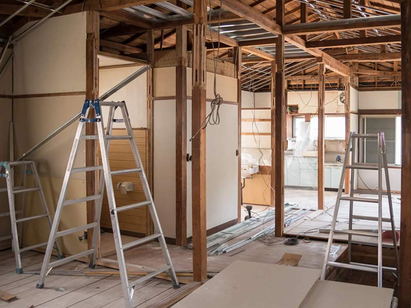Home interior under renovation with exposed wooden framing, ladders, and construction materials scattered around.