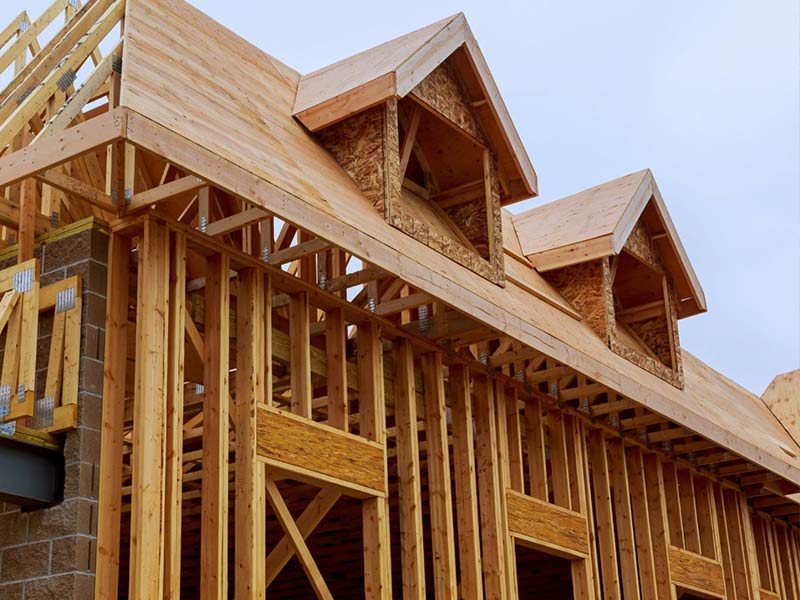 Wood framing of a house under construction, featuring dormer windows on the roof.